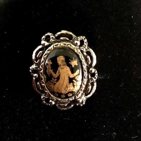 A vintage-style cameo pin featuring an intricate gold-tone etching of a maiden against a black background, framed in ornate silver-tone detailing.