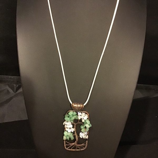 Embrace nature’s elegance with our Enchanted Blossoms Tree Necklace, featuring a tree of life pendant adorned with green and white stones on a sleek white cord. Perfect for any outfit, from bohemian to evening chic.