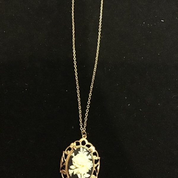 The Midnight Bloom Cameo Necklace features a striking ivory floral design against a deep black background, framed in an ornate gold-tone setting. A timeless statement piece with vintage charm!